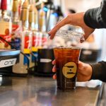 A Ziggi's Coffee barista putting the top of an iced coffee behind the service bar.
