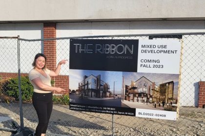gajiza dumplins owner standing next to the ribbon in detroit construction site sign