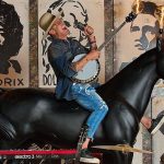 Chef Brian Malarkey playing banjo sitting atop a horse statue